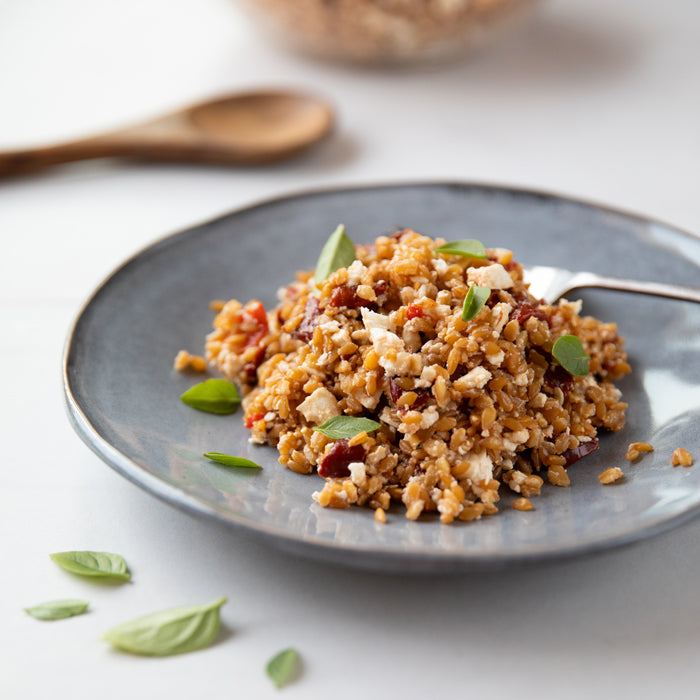 Roasted red pepper and einkorn wheat berry salad on a blue ceramic plate with crumbled feta and fresh basil