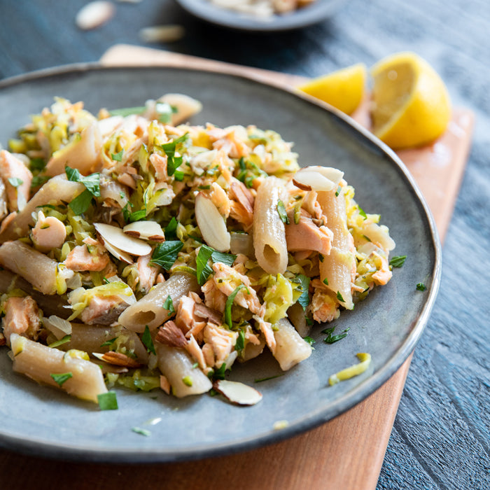 Salmon and zucchini gluten free cassava pasta served on a gray plate with sliced almonds and lemon wedge on a wooden board