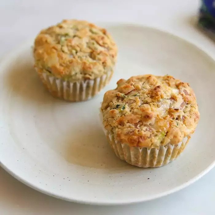 Top-down view of two ham and cheese Einkorn zucchini muffins showcasing shredded zucchini and golden baked tops on a white plate