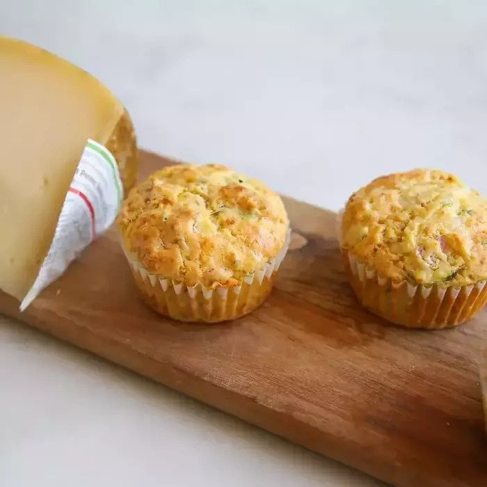 Front view of two Einkorn zucchini muffins with golden, cheesy tops and zucchini flecks on a wooden cutting board