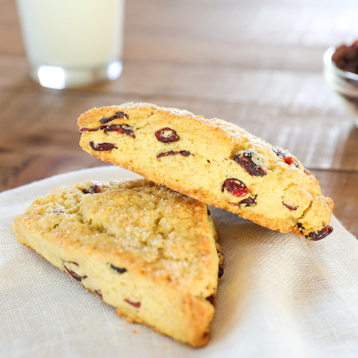 Close-up of two Einkorn orange cranberry scones with cranberries and sugar-dusted tops on a cloth