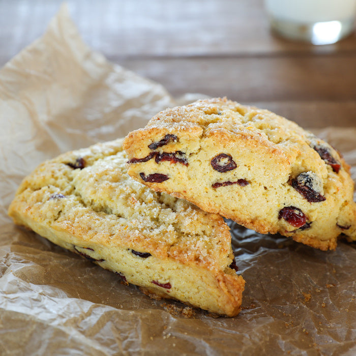 Close up of two halved einkorn orange cranberry scones showing golden crumb studded with cranberries on parchment