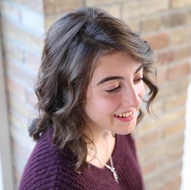 Smiling young woman in a purple sweater looking down in three-quarter profile against a brick wall background