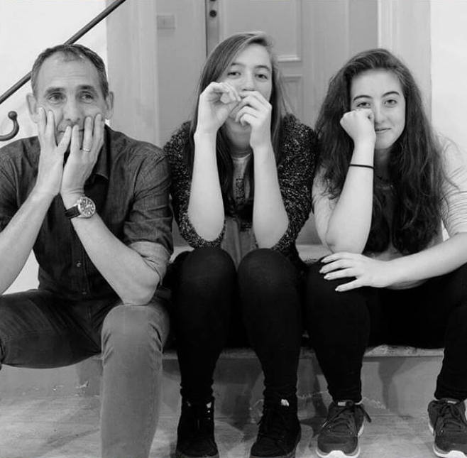Founders posing with two daughters seated on indoor steps, leaning on their hands in a casual black-and-white portrait