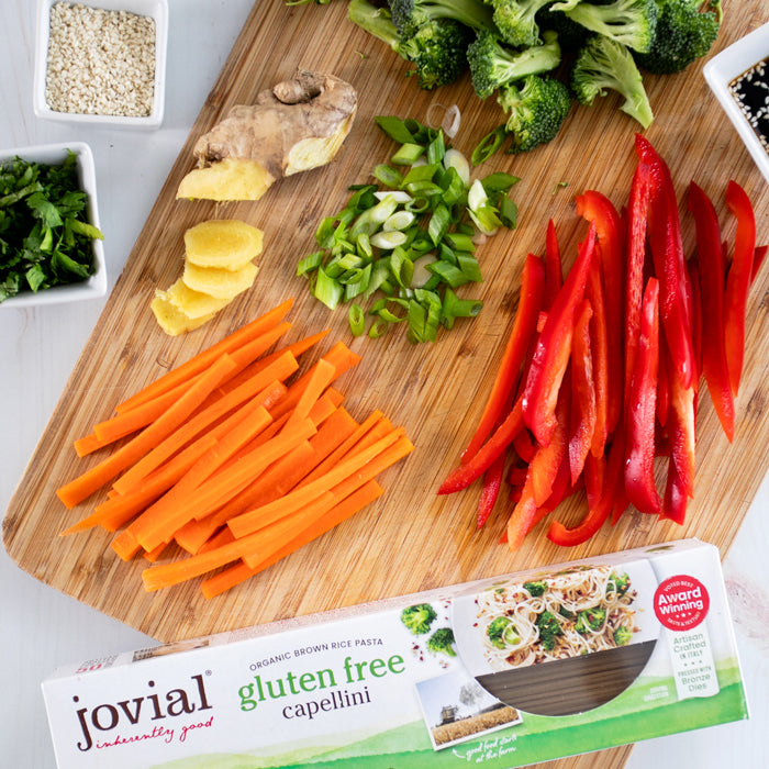 Ingredients for sesame scallion ginger noodles arranged on a cutting board with a Jovial gluten free capellini box