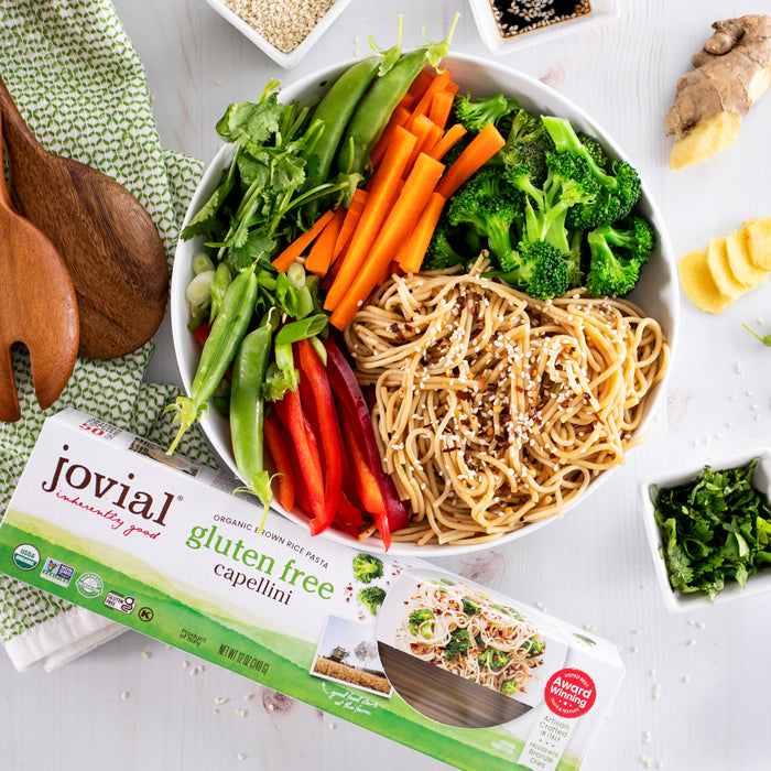 Top-down view of Jovial gluten-free capellini box with a bowl of ginger sesame noodles garnished with sesame seeds and vegetables