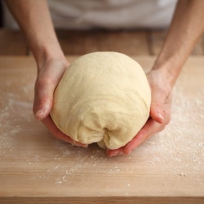 Hands shaping a ball of einkorn sourdough dough on a floured wooden board