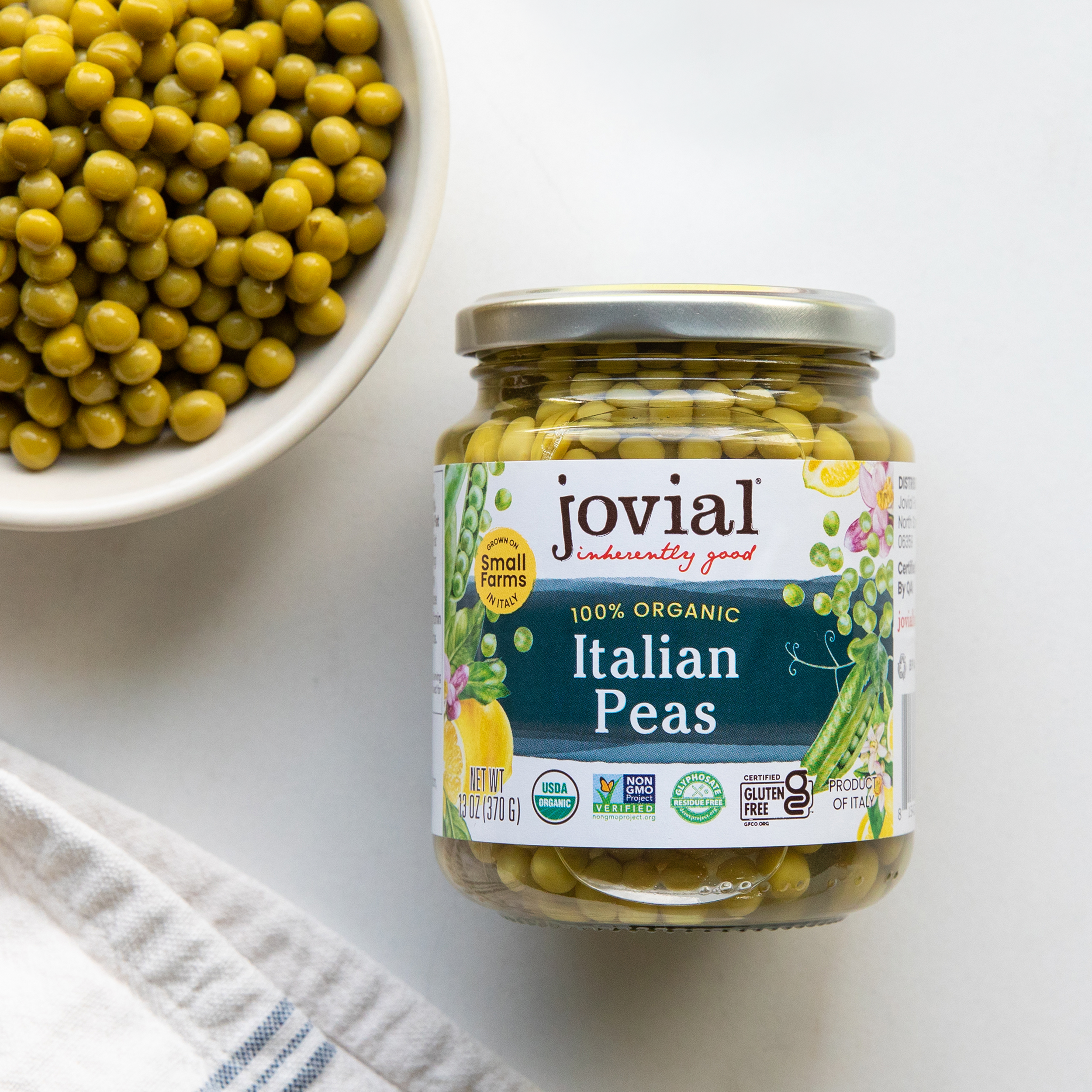 Front view of Jovial Italian Peas jar showcasing 100 percent organic label and certified gluten free badge with a bowl of peas on a white background
