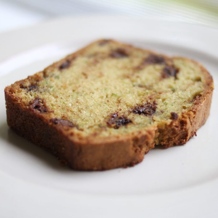 Angled slice of Einkorn zucchini bread with chocolate chips showing green zucchini flecks and golden crust on white plate