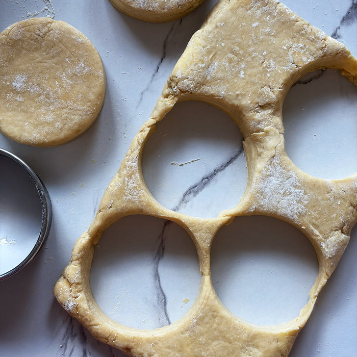 Round einkorn sourdough biscuits being cut from rolled dough on a floured marble surface with a metal cutter