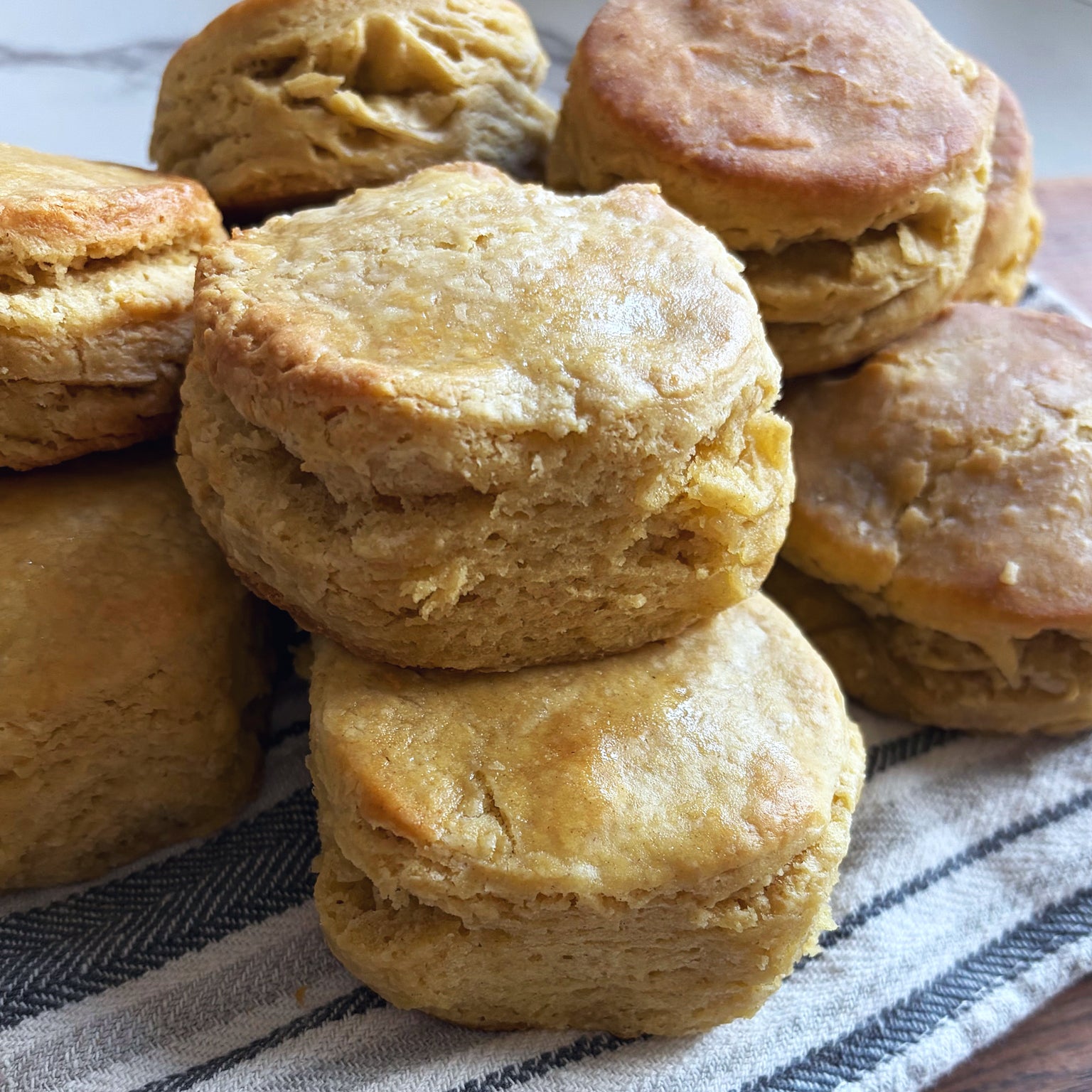 Close-up of stacked einkorn sourdough biscuits showcasing flaky, layered interior and golden-brown tops on a striped cloth