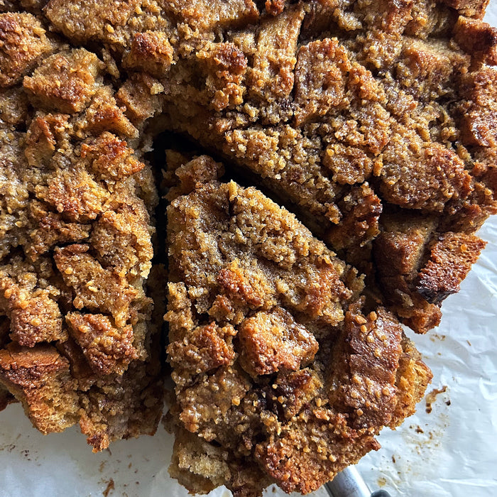 Close-up of maple caramel sourdough einkorn bread pudding showcasing a golden crumbly topping and a sliced wedge on parchment
