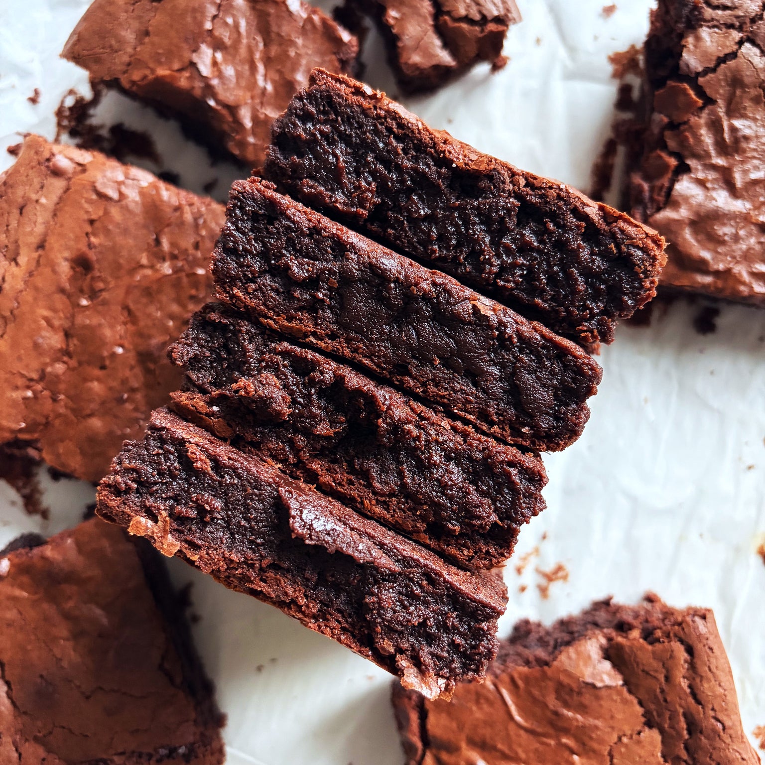Overhead close-up of sourdough einkorn brownies showcasing fudgy, dense interior and cracked shiny top on parchment paper