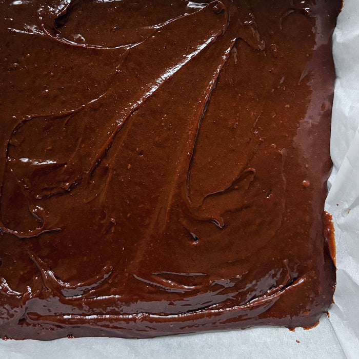 Sourdough einkorn brownie batter smoothed in a parchment-lined baking pan ready for baking
