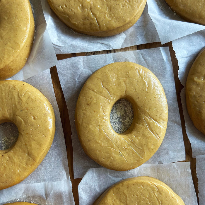 Top-down view of sourdough donut dough rings showing smooth, glossy surface and central holes on parchment over wood board