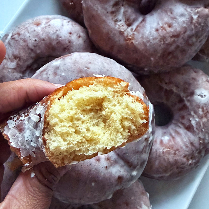 Close-up of sourdough donut torn open showcasing airy interior and sugar glaze with more glazed donuts on a white platter