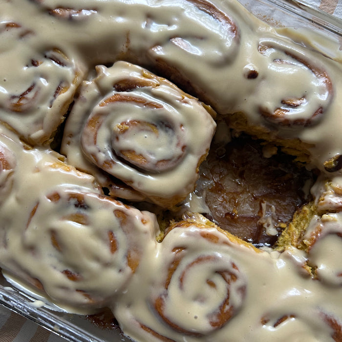 Close-up of sourdough pumpkin cinnamon rolls in a glass baking dish showcasing cinnamon swirls and maple cream cheese frosting