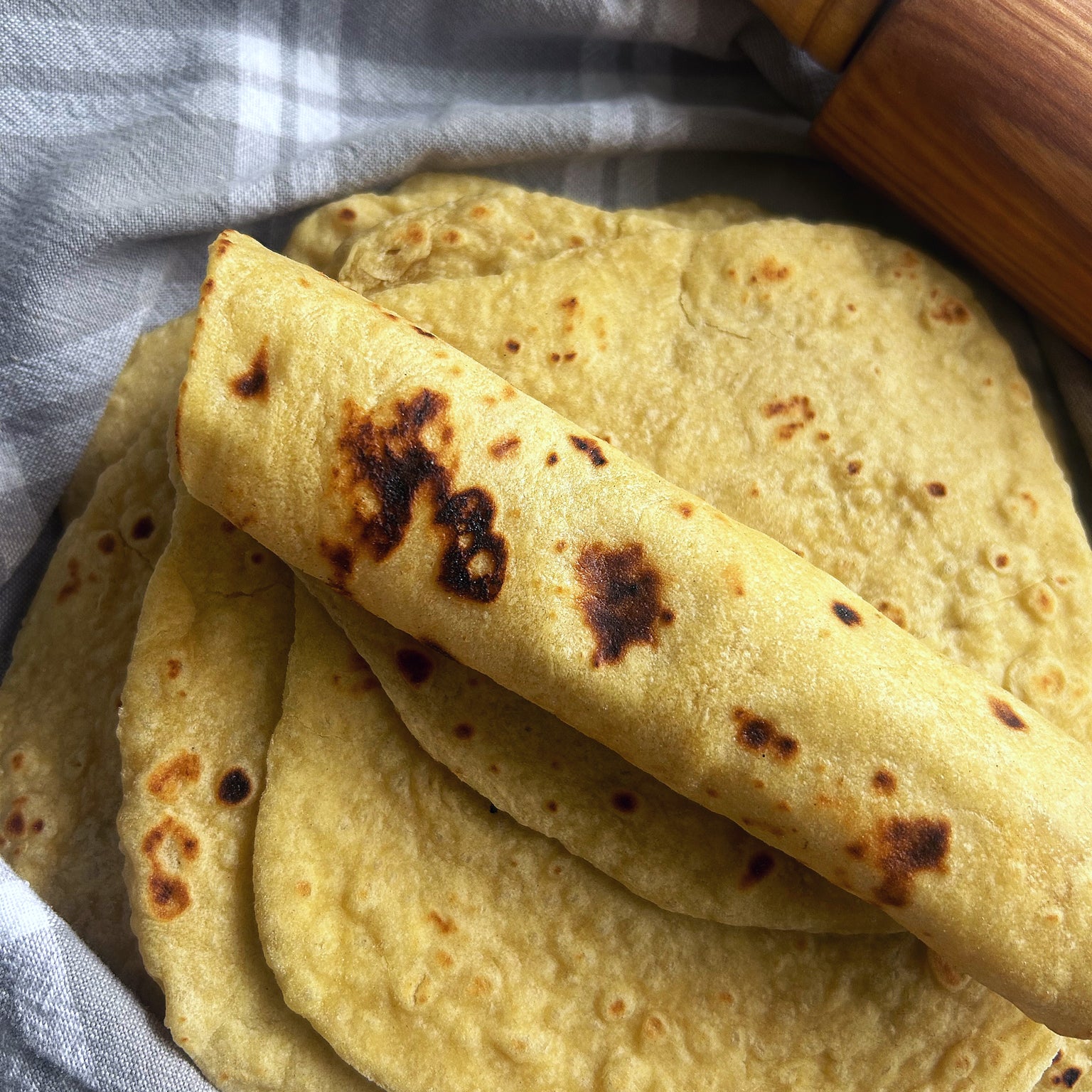 Close-up of einkorn sourdough tortillas showcasing charred brown spots and soft folded stack on a gray cloth