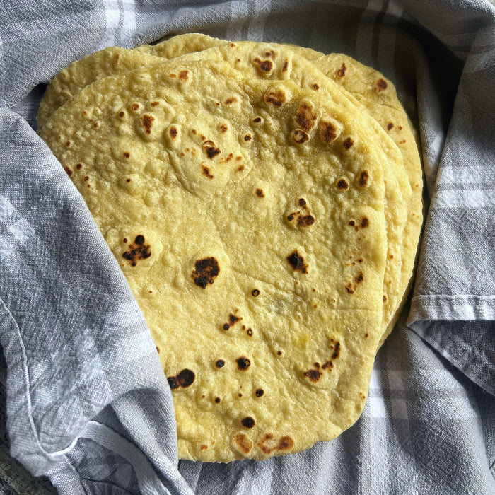 Top-down view of einkorn sourdough tortillas showing golden char spots and soft, pliable texture wrapped in a gray checkered towel
