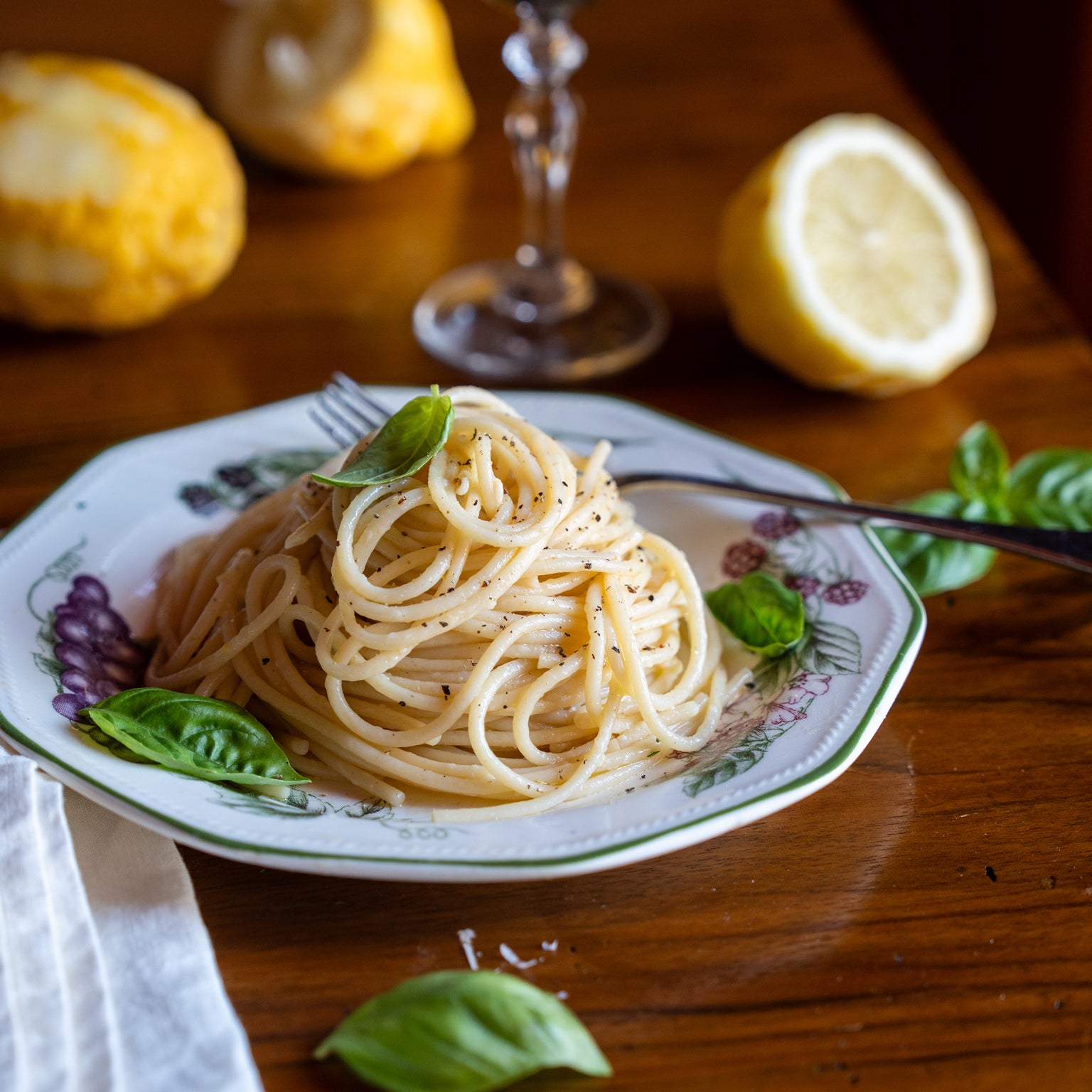 Spaghetti al limone twirled on a fork on a plate, garnished with basil, lemon halves on a wooden table