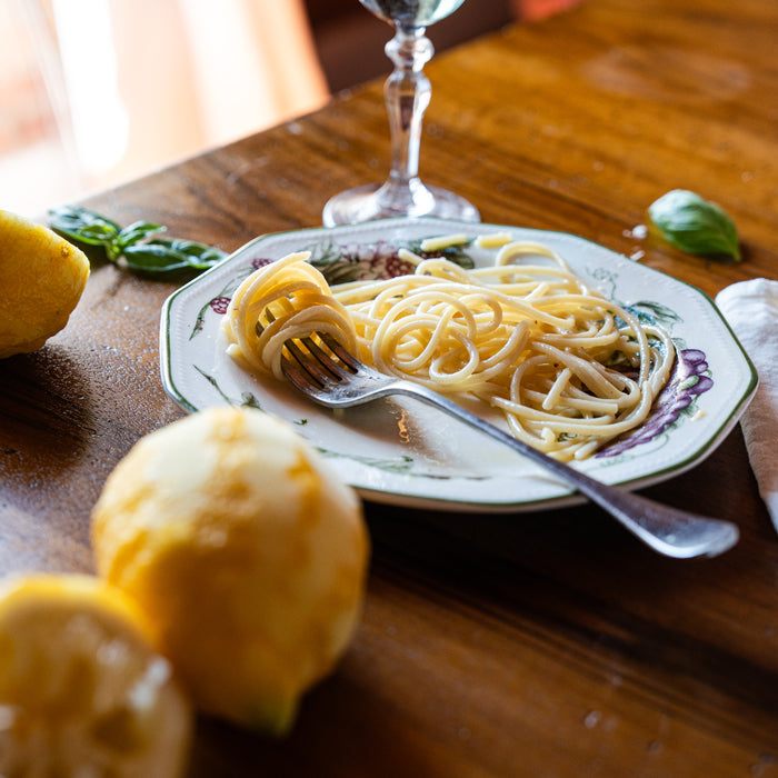 Fork twirling spaghetti al limone on a decorative plate with lemon and basil on a wooden table in warm natural light