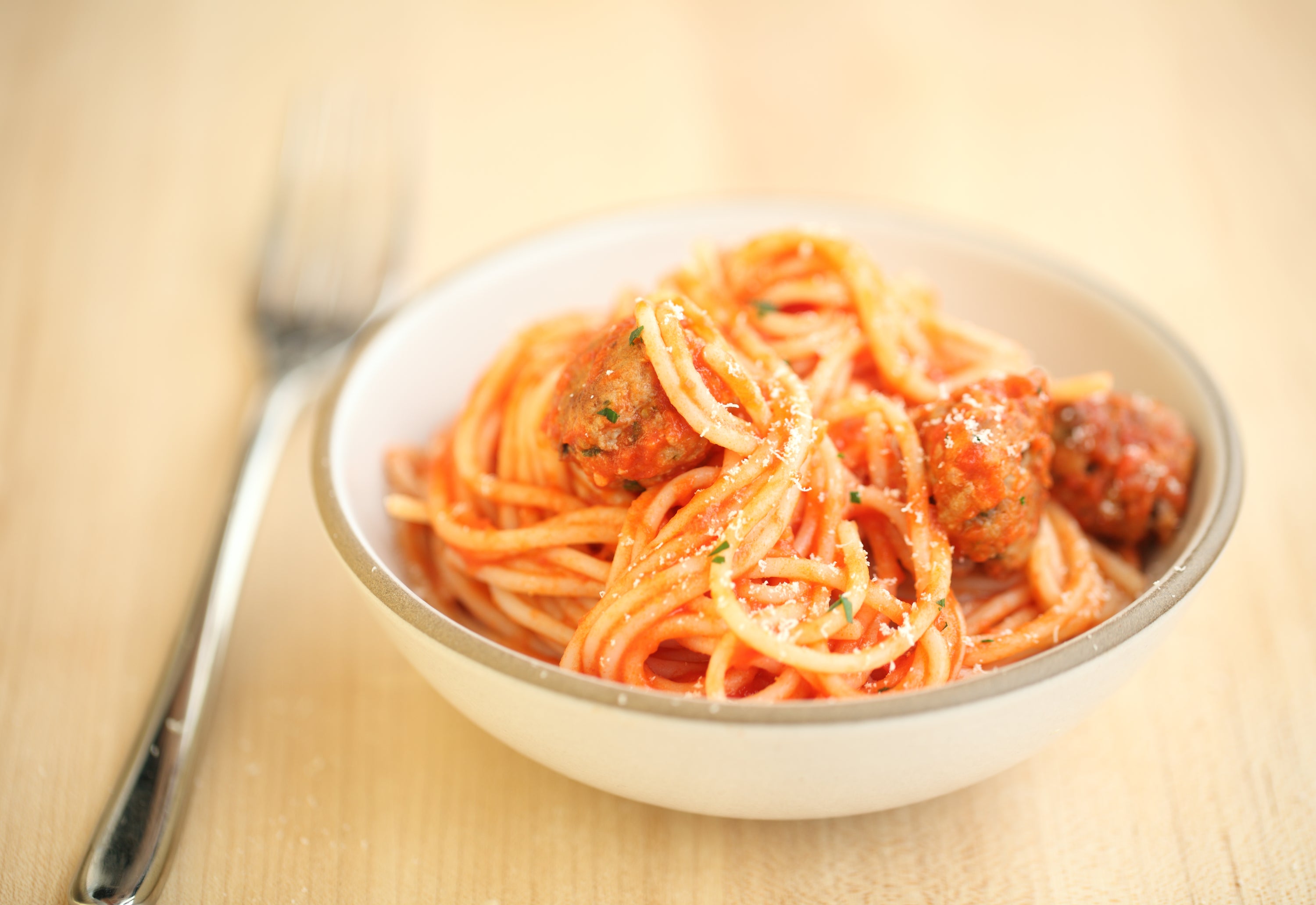 Close-up of bowl of spaghetti and gluten-free meatballs in tomato sauce with grated cheese and fork on wooden table