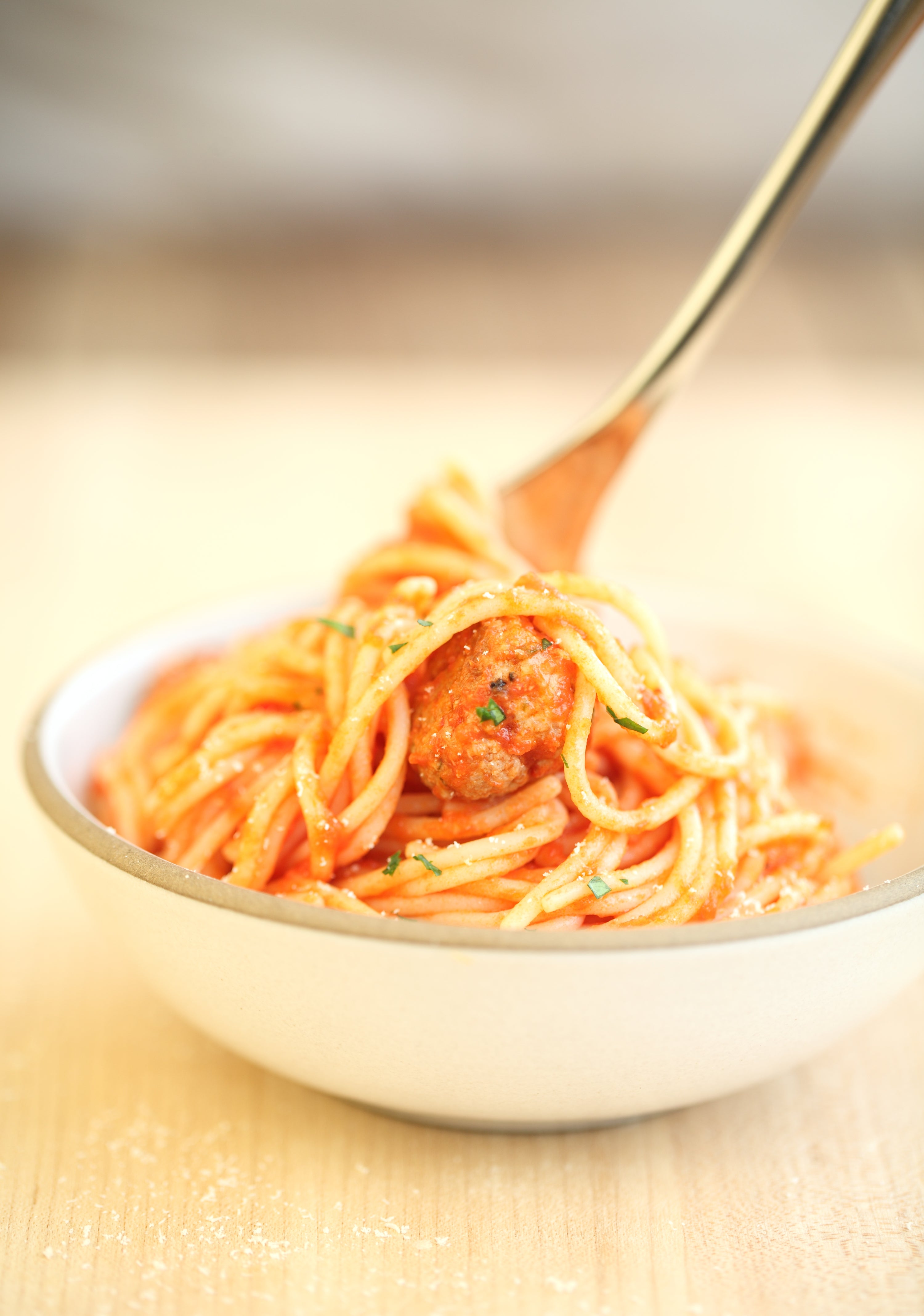Fork twirling spaghetti and a gluten-free meatball in a bowl of tomato sauce on a wooden table