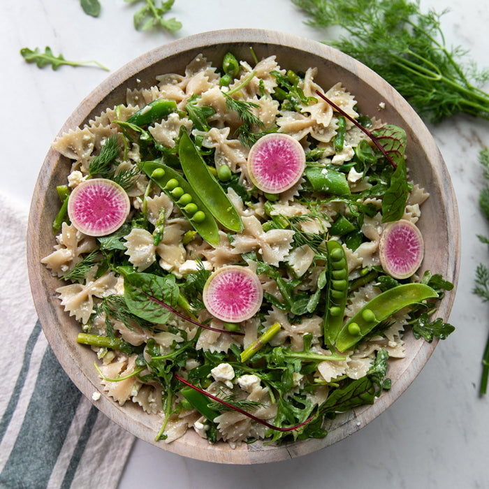 Top-down spring pasta salad with gluten-free brown rice farfalle, asparagus, snap peas, arugula, dill, and feta