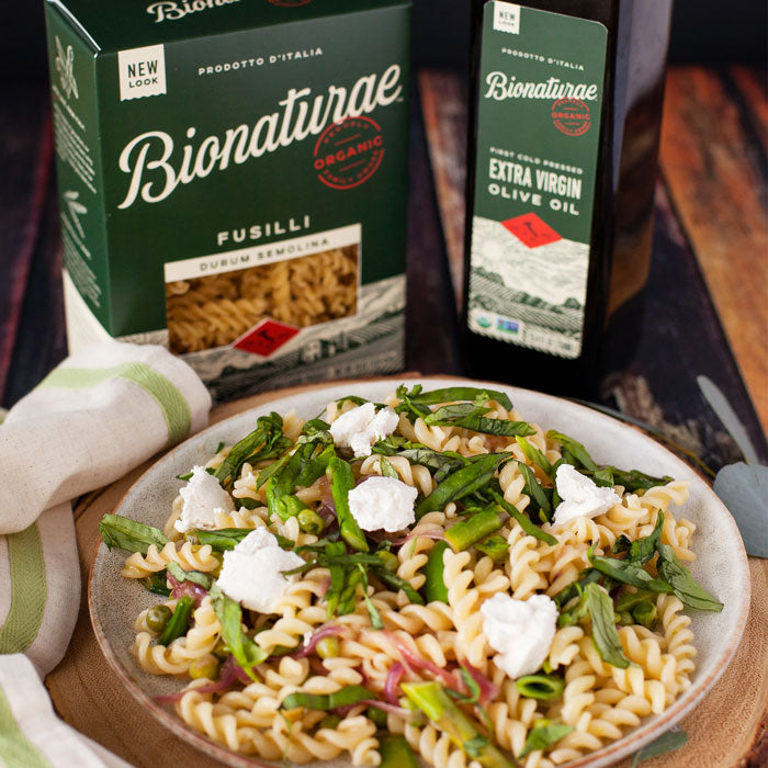 Bowl of spring vegetable fusilli with asparagus, peas, basil, and cheese, Bionaturae fusilli box and olive oil bottle behind
