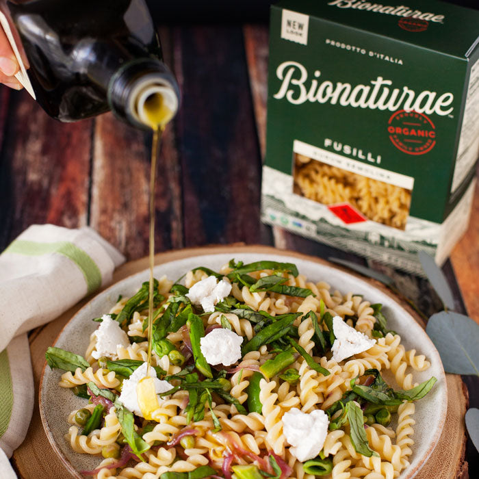 Bowl of fusilli with peas, asparagus, basil, and goat cheese, olive oil being poured, Bionaturae fusilli box behind