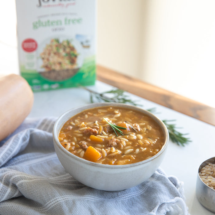 Bowl of autumn squash and orzo soup with sausage served on a cloth-lined table, Jovial gluten-free orzo box blurred in the background