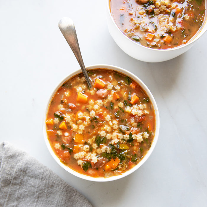 Bowl of tomato vegetable soup with organic gluten-free brown rice stelline pasta, spoon and napkin on marble surface