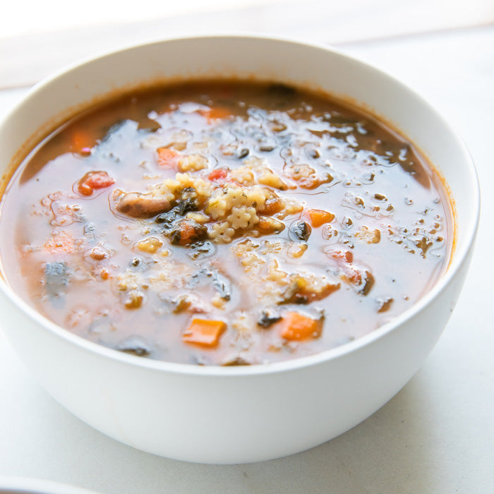 Top-down view of a bowl of Stelline minestrone soup with brown rice stelline pasta, carrots, borlotti beans, and spinach
