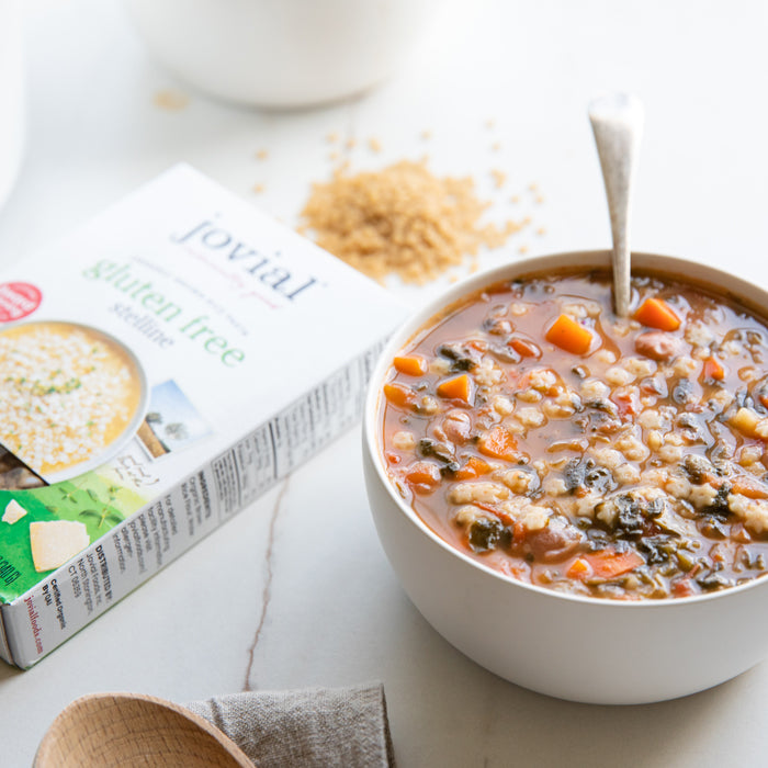 Bowl of vegetable and borlotti bean soup with tiny star-shaped Jovial brown rice stelline pasta and box in background