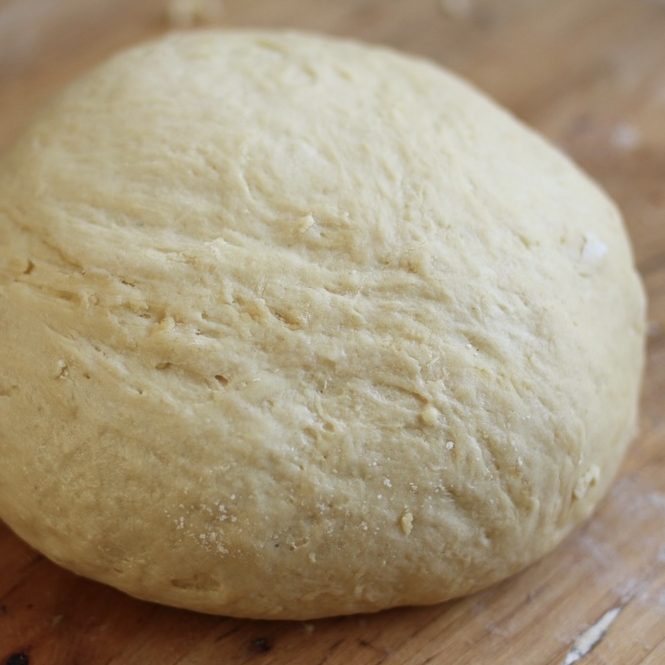 Top view of a round einkorn sandwich bread dough ball showing a smooth, slightly sticky surface on a wooden board