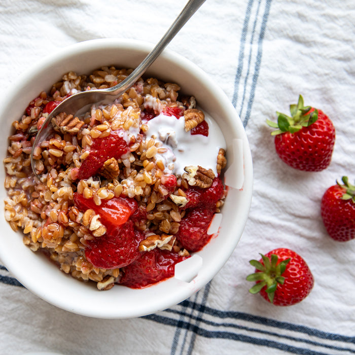 Bowl of strawberries-and-cream Einkorn wheat berries topped with coconut cream and chopped pecans on a striped cloth
