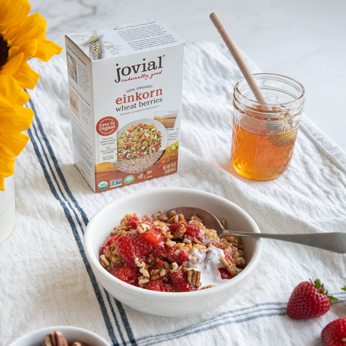 Bowl of strawberries and cream wheat berries with coconut cream, spoon, Jovial einkorn wheat berries box and jar of honey