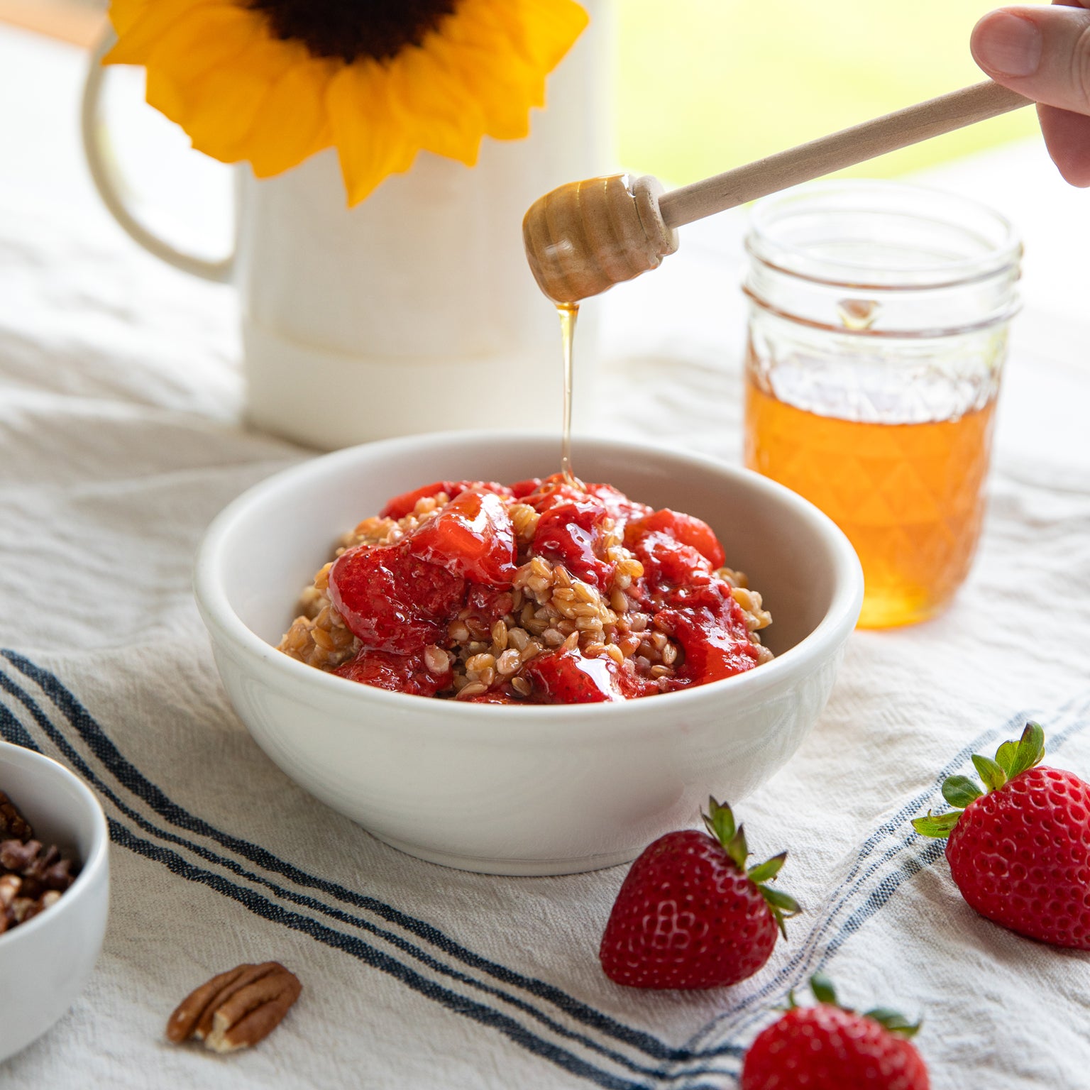 Bowl of einkorn wheat berries topped with sautéed strawberries and honey drizzle on a white linen tablecloth