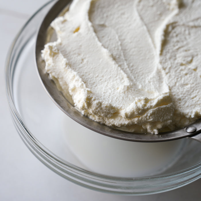 Ricotta cheese draining in a mesh sieve, over a bowl