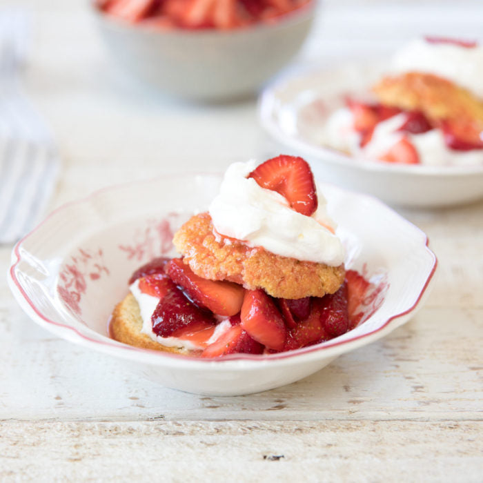Close-up of Einkorn strawberry shortcake with macerated strawberries and whipped cream in a white bowl on a light wooden table