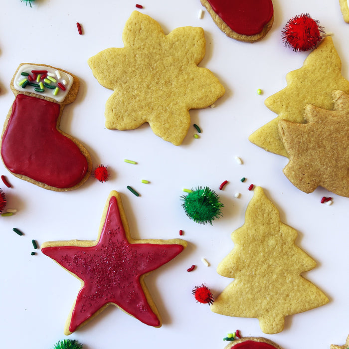 Top-down view of sourdough einkorn sugar cookies shaped like stars, trees, and stockings, some with red icing and sprinkles