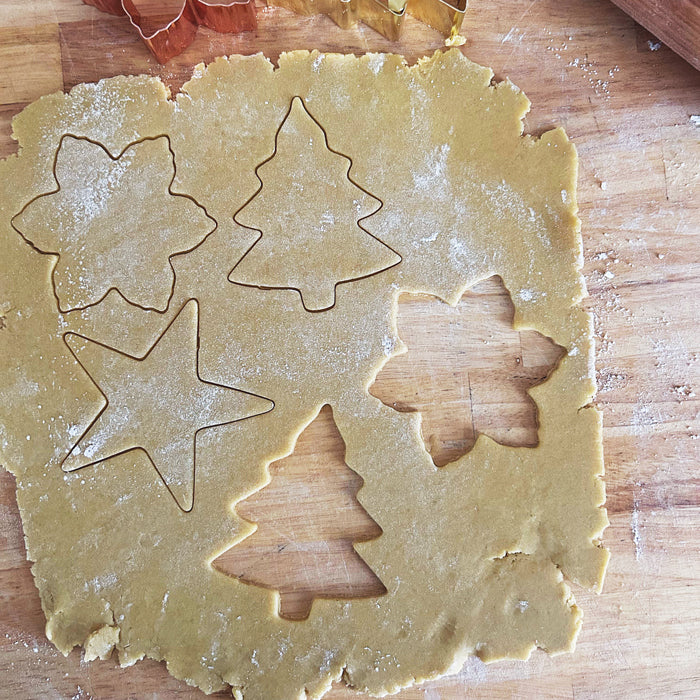 Sourdough einkorn sugar cookie dough cut into tree, star, and flower shapes on a floured wooden board