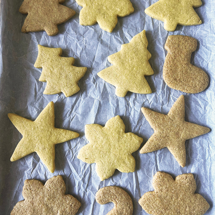 Overhead view of sourdough einkorn sugar cookies cut into stars, trees, stockings, and flowers on a parchment-lined baking sheet