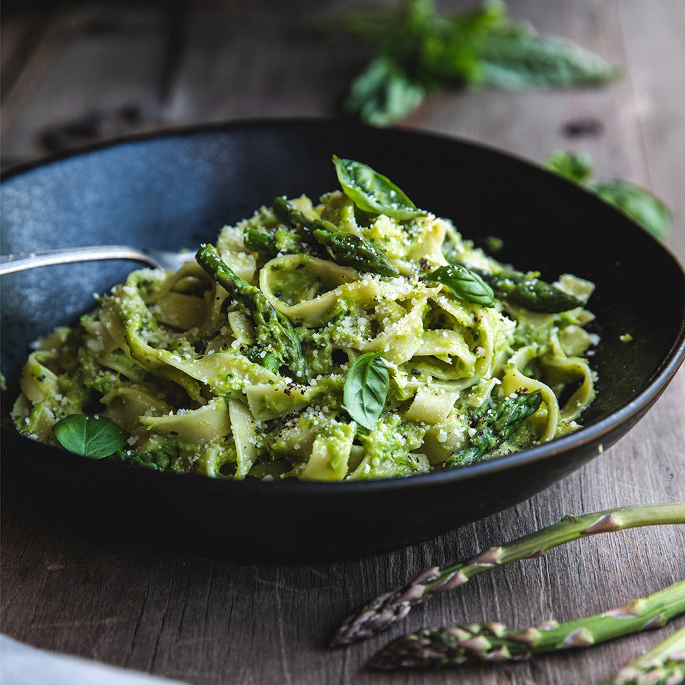 Close-up of Organic Traditional Egg Tagliatelle with asparagus pesto, asparagus tips, basil, and grated cheese in a black bowl