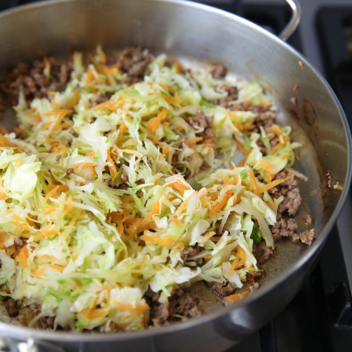 Skillet of ground meat with shredded cabbage and carrots stir-frying on the stovetop for teriyaki brown rice pasta