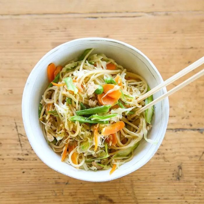 Top-down view of teriyaki brown rice pasta stir fry in a white bowl with cabbage, carrots, and snap peas