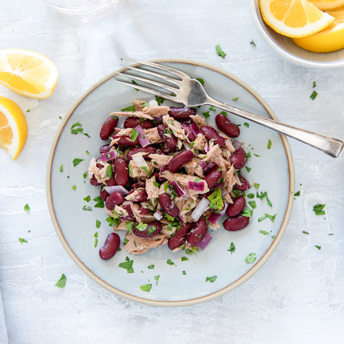 Top-down view of tuna and kidney bean salad with flaked tuna, red kidney beans, chopped red onion, and parsley on a pale blue plate