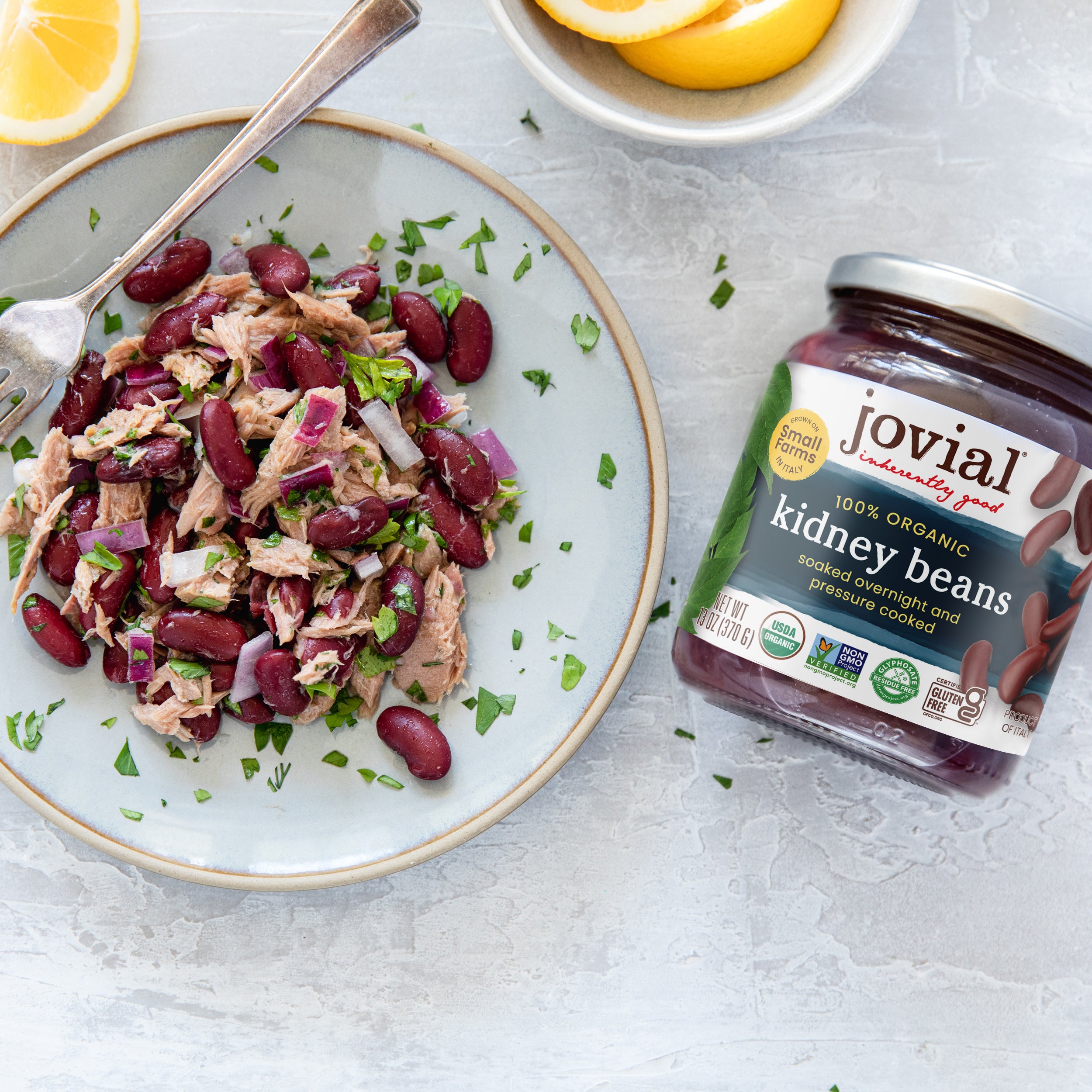Front view of Jovial organic kidney beans jar beside a plate of tuna and kidney bean salad on a light marble surface