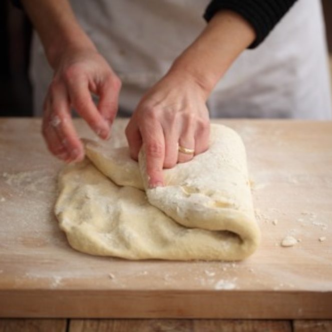 Hands folding sourdough dough on a floured wooden board while preparing an Einkorn artisan loaf