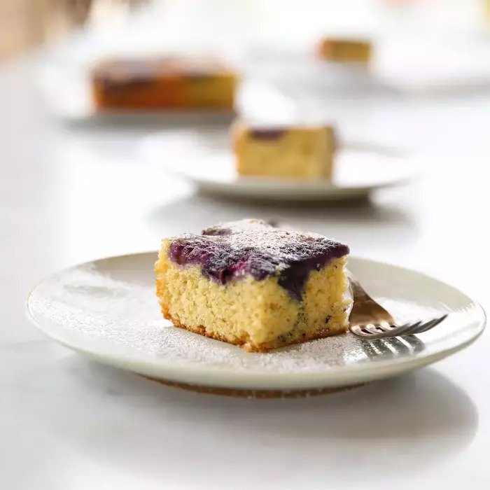 Close-up of an Einkorn blueberry upside-down cake slice showing moist crumb, blueberry topping, and powdered sugar on a white plate